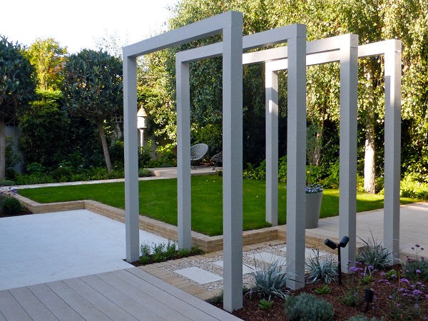 Large garden with modern metal colonnade and landscaping of Millboard composite decking, Sandy White porcelain paving and grass.