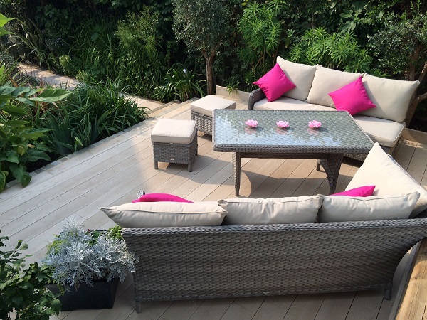 Outdoor sofas and table on Limed Oak Millboard composite decking patio, edged with plants.