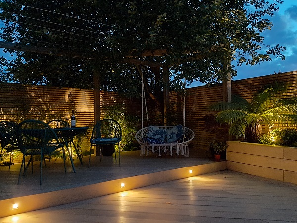 Illuminated corner of garden with Amber DesignBoard composite decking  with step up to seating area.