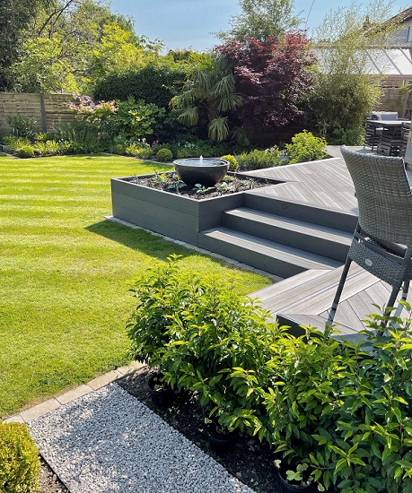 Charcoal DesignBoard composite deck with 3 steps descending to lawn on 2 sides.