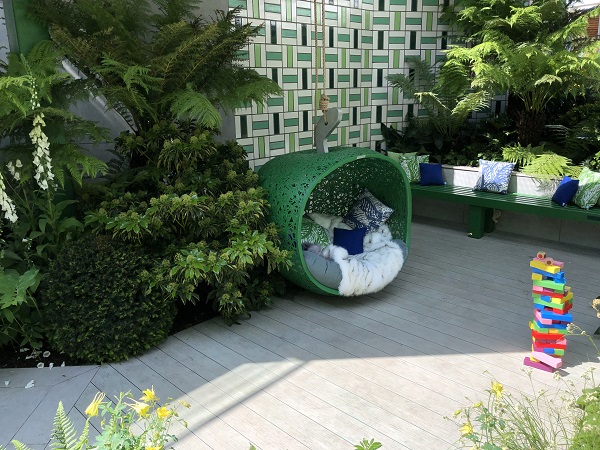 Small seating pod on DesignBoard composite decking in wheelchair accessible garden with bench, tall ferns and tiled wall.