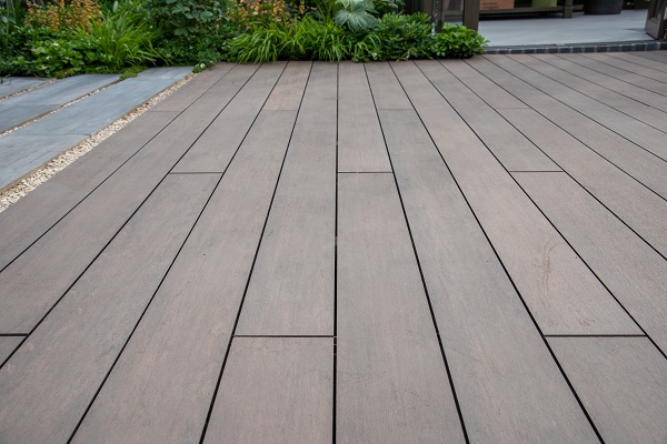 View down length of Chestnut Brushed budget composite decking to foliage in planted border.