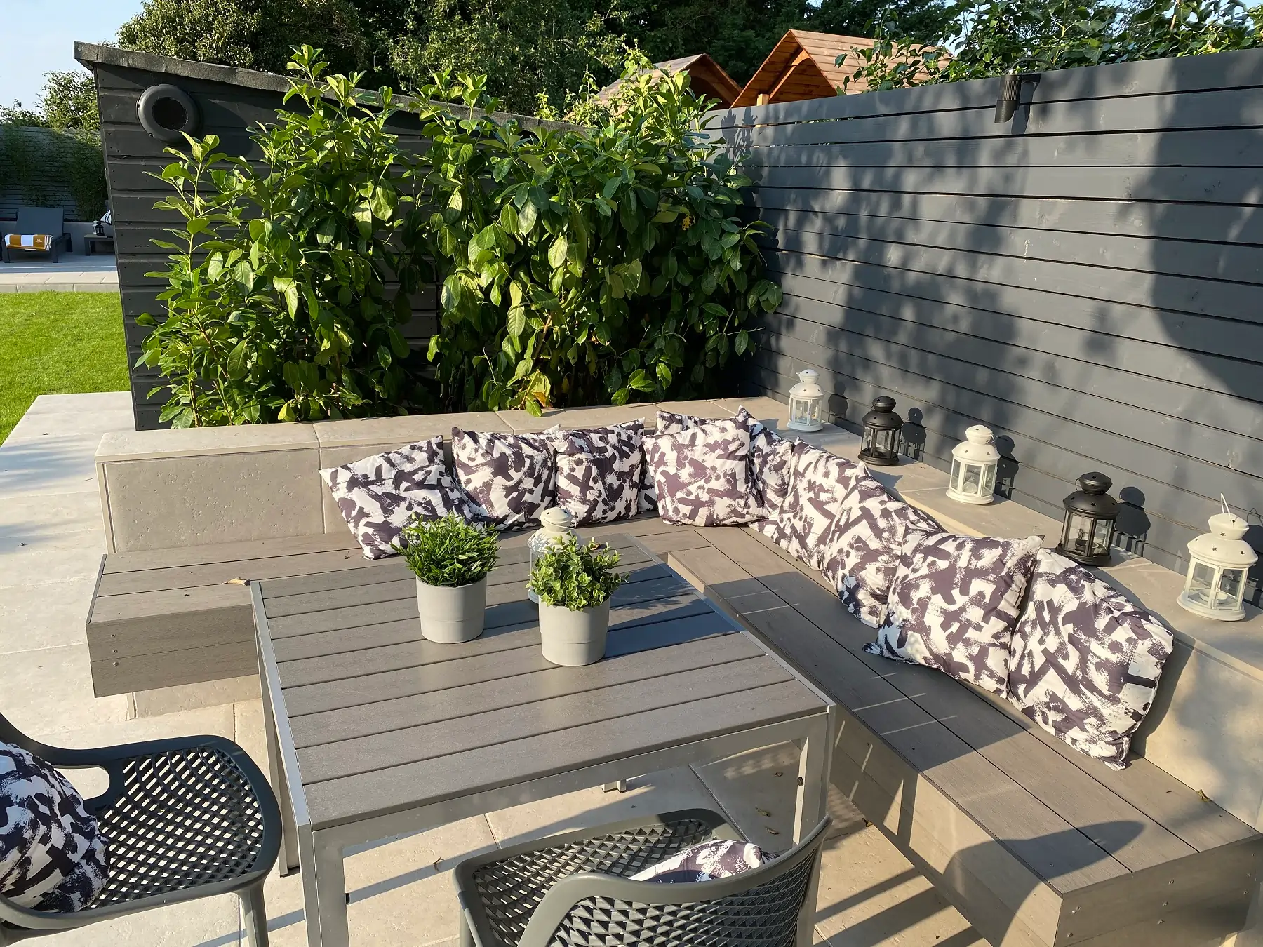 Pebble Grey and Dark Ash budget composite decking used as corner bench, table and fence , with cherry laurel hedge hiding shed.