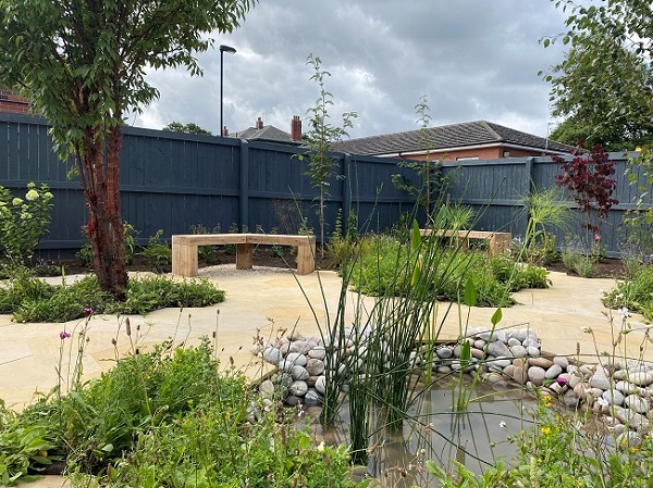 Radio 2 Bee garden with reeds in pond edged with large pebbles and paving of hexagonal slabs of Dune sawn sandstone.