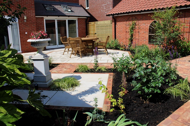 Back garden with Venetian Beige paved areas divided by Cotswold brick pavers. Seating next to patio doors. 