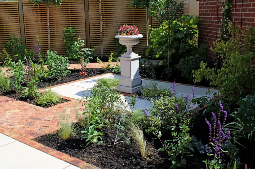 Flower filled urn on pedestal in symmetrical paved area of Venetian Beige porcelain paving edged with clay pavers.