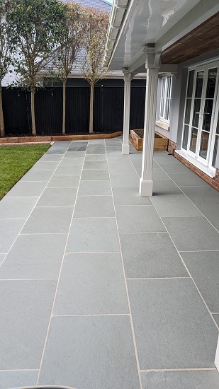 Graphite Grey limestone patio runs across back of house with white doors. 