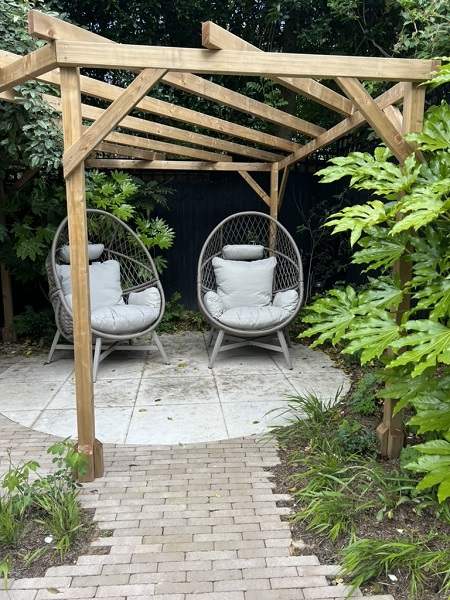 Stone Grey clay pavers lead to Florence White porcelain paved circle under wooden pergola with 2 seats. 