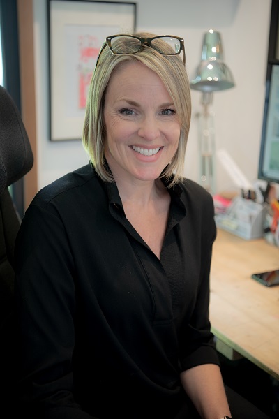 Karen McClure, woman with fair hair, sits smiling at camera
