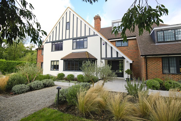 Large house with patio of urban grey porcelain paving and gravel, with grasses in beds.