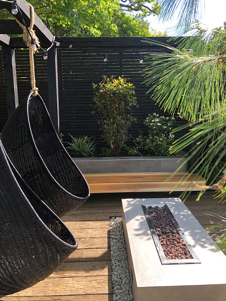 2 egg chairs hang from beam in front of rectangular fire table on Millboard Vintage Oak planking. Fence in background.