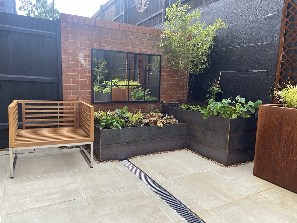 Cream porcelain budget paving in small courtyard with mirro on wall and raised beds. 