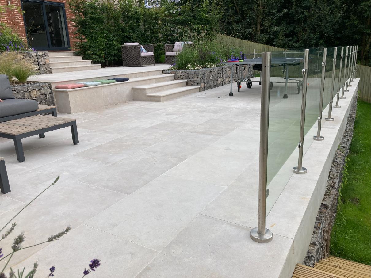 Terraced Egyptian beige limestone patio descend from house via matching steps, with raised beds of stone-filled gabions.